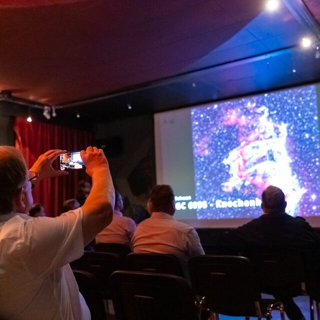 Im Vortragsraum wird eine Aufnahme auf der Leinwand gezeigt.
